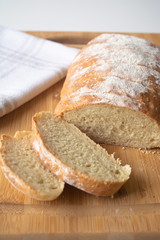 A loaf of homemade fresh bread with flour sprinkled on top in a kitchen towel on wooden cutting board with slices
