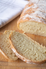 A loaf of homemade fresh bread with flour sprinkled on top in a kitchen towel on wooden cutting board with slices