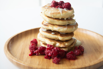 Fluffy pancakes with condensed milk and raspberries on a wooden plate with a kitchen napkin and a fork 