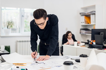 Young attractive male fashion designer leaning on the office desk, working on a sketch