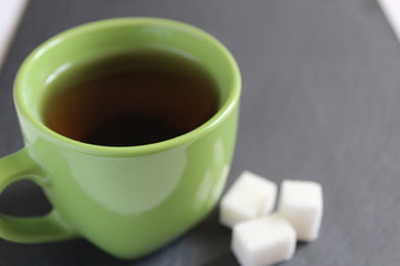 tea in a green Cup mug stands on a gray stone black background next to three pieces of sugar with a...
