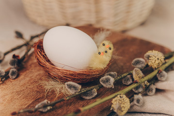 Easter white egg with little chick toys in nest on a wooden board in rustic style, close-up.