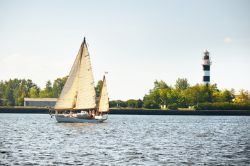 Old vintage wooden sailboat (yawl) close-up, sailing on a clear day. Lighthouse in the background....
