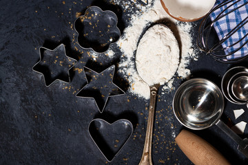 spoon with flour, forms and ingredients for baking on a black background, closeup