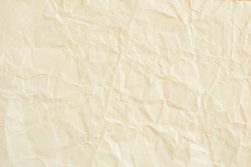 Crumpled beige sheet of paper with rough surface texture background.