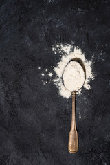 spoon with wheat flour on a black background, vertical