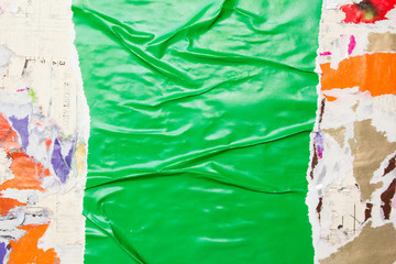 Torn and crumpled green glossy paper poster glued on surface with old peeling pieces of paper placards texture background. Copy space for text.