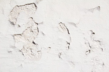 Old weathered white wall with rough surface and peeling paint and plaster texture background.