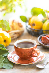 Cup of tea with homemade quince jam on an old wooden background. Fresh fruits and quince leaves on the background.