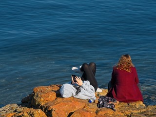 Two girls sit in the sun at the spectacular rocky shore of Sidney BC, Vancouver Island