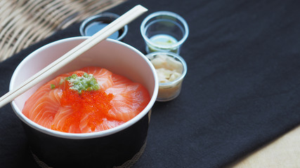 Top View and focus on Salmon with Japanese rice or Salmon Ikura Don in paper dish from delivery restaurant on black Table cloths