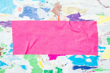 Pink piece of cloth fluorescent gaffer tape on billboard with torn and crumpled colorful paper posters background. Copy space for text.