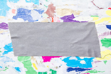 Grey piece of cloth gaffer tape on billboard with torn and crumpled colorful paper posters background. Copy space for text.