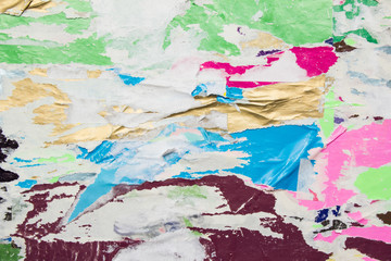 Bright colorful torn crumpled and peeling paper glued on rough surface. Closeup old dirty urban billboard background.