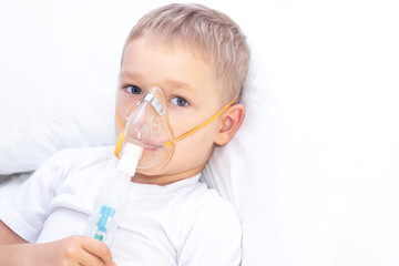 boy with an inhaler mask - respiratory problems in asthma. a boy with an inhaler mask lies in bed and breathes adrenaline. healthcare concept and sick child, coronavirus, bronchitis, pneumonia