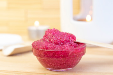 Natural pink body scrub made from sugar. Pink scrub in a glass cup on a background of candles and sugar.