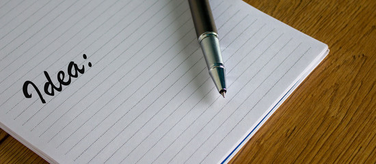 Notebook with the inscription idea and pen on wood table.