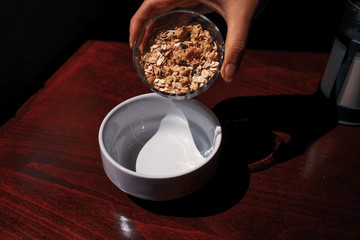 Pouring the oatmeal into the white porcelain bowl standing on wooded table.
pouring oatmeal for breakfast in a white porcelain oatmeal bowl. preparing for the breakfast with oatmeal.