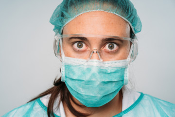 Close up of a Young woman doctor wearing medical mask, glasses, latex gloves and protective clothing against the virus on white background. COVID-19 The coronavirus pandemic.