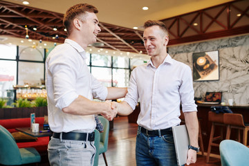 Naklejka premium Cheerful young business people shaking hands after successful meeting in cafe