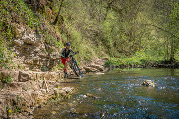 pretty mid age woman riding her mountainbike at a little river on a warm sunny spring day