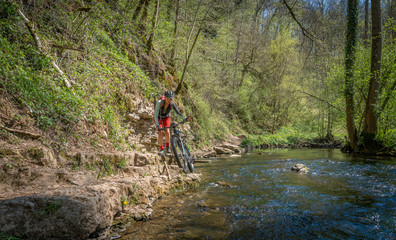 Fototapeta premium pretty mid age woman riding her mountainbike at a little river on a warm sunny spring day
