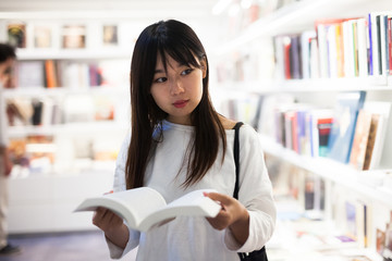 Young female student choosing new books on shelves