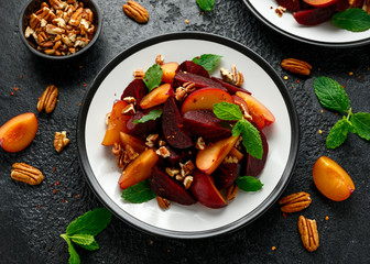 Vegan Plum, beet salad with pecan nuts, mint and herbs on rustic black table