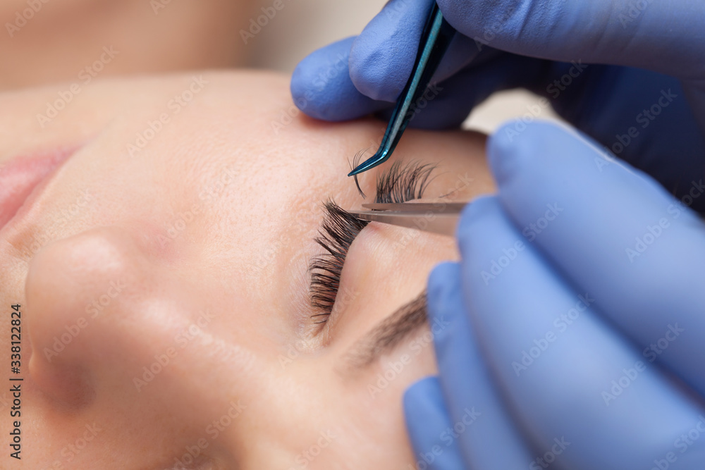 Wall mural Eyelash extension procedure close up. Beautiful woman with long eyelashes in a beauty salon. Makeup concept