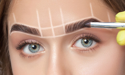 The make-up artist applies a henna paints eyebrow dye on the eyebrows of a young girl. Professional...