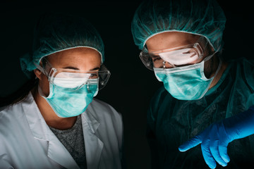 Portrait of Close up of two woman and man doctors working wearing medical surgical mask, glasses, medical cap and virus protective clothing on black background with copy space. 