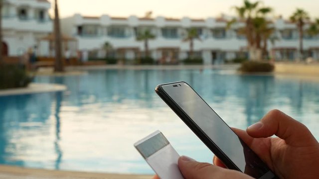 Buy something online with smartphone and credit card near swiming pool on vacation