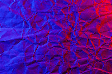 Crumpled craft paper texture in neon red blue light. Solid background.