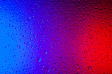 Drops of water on glass in red-blue neon light. Rain on the glass against the background of two colored lights. Abstract photo for background.