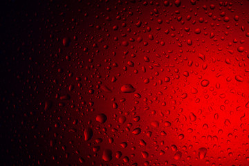 Drops of water on glass in red neon light. Rain on the glass against the background of colored lights. Abstract photo for background.