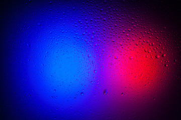 Drops of water on glass in red-blue neon light. Rain on the glass against the background of two colored lights. Abstract photo for background.