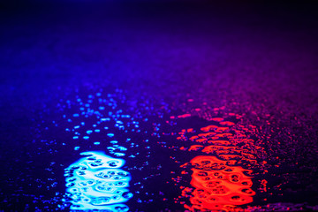 Abstract photo reflection of light on a wet surface. Blue and red neon light on a textured wet surface. Reflection of light on the pavement. Glare on the water.