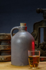 Shot Glass with Whiskey in Background a Vintage Stoneware Crock and Tools