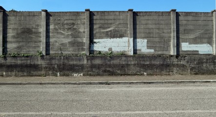 Grunge concrete wall with erased graffiti in the suburbs. A sidewalk and an asphalt road ahead. Background for copy space.