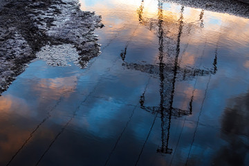 Reflection in puddle of transmission tower on cloudy sky background in springtime, selective focus.