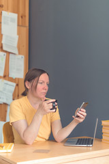 Female freelancer working on smartphone and drinking coffee