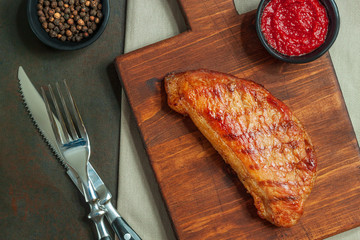 Grilled beef steak with spices on cutting wooden board and cutlery.