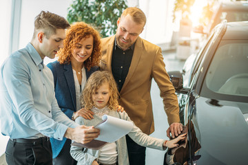 young caucasian family consisted of man, woman and child in dealership, they are going to make purchase, to buy new automobile. family choose the best variant, examining all details © alfa27