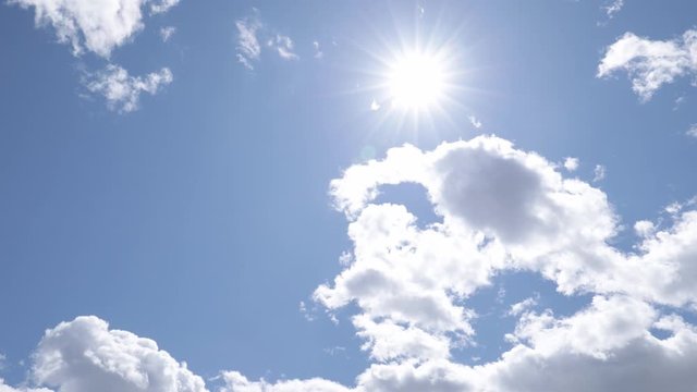 Slow camera movement cross sunny blue sky with white clouds, lens flare, looking into the sun, 4k