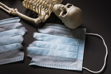 Skeleton and medical mask torn in half. COVID-19 Pandemic Mortality Concept