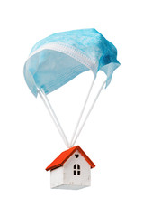A toy house is flying on a parachute from a medical mask, isolated on a white background. The...