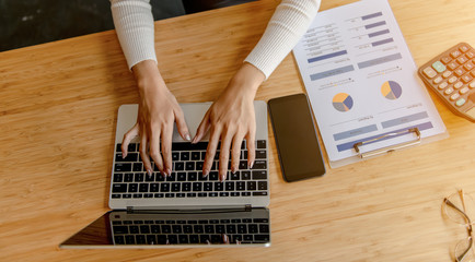 Asian woman uses a laptop at home while sitting at a wooden desk, hand typing on a notebook keyboard, the concept of young people work from home