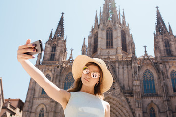 Fototapeta premium Young and happy tourist woman making selfie photo in front of cathedral in Barcelona