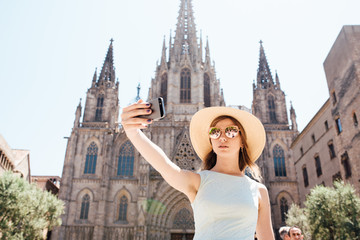 Fototapeta premium Young and happy tourist woman making selfie photo in front of cathedral in Barcelona