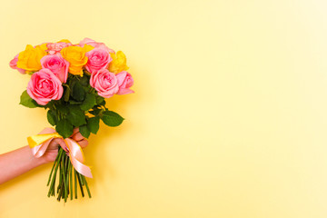 holding beautiful tender blossoming bouquet of yellow and pink roses on yellow background. Free copy space. Flowers delivery at home.